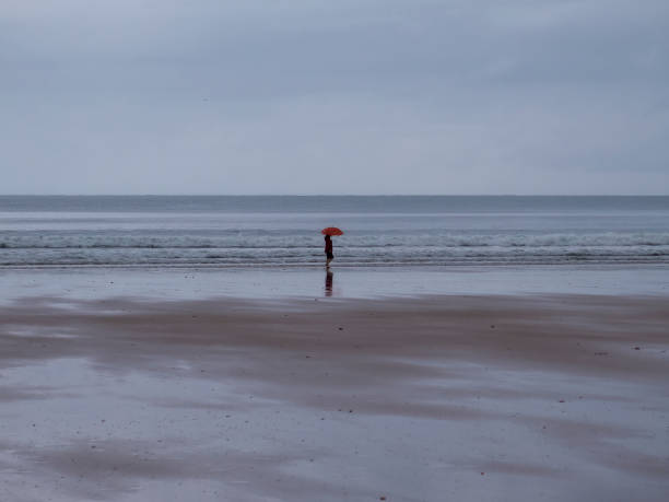 istock woman walking along the seashore with umbrella 1419270086