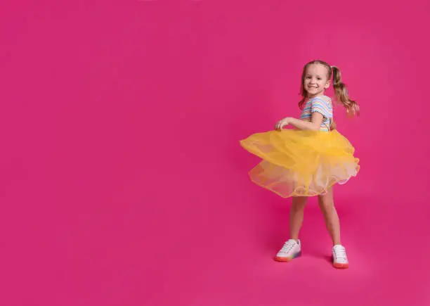 Cute little girl in tutu skirt dancing on pink background. space for text