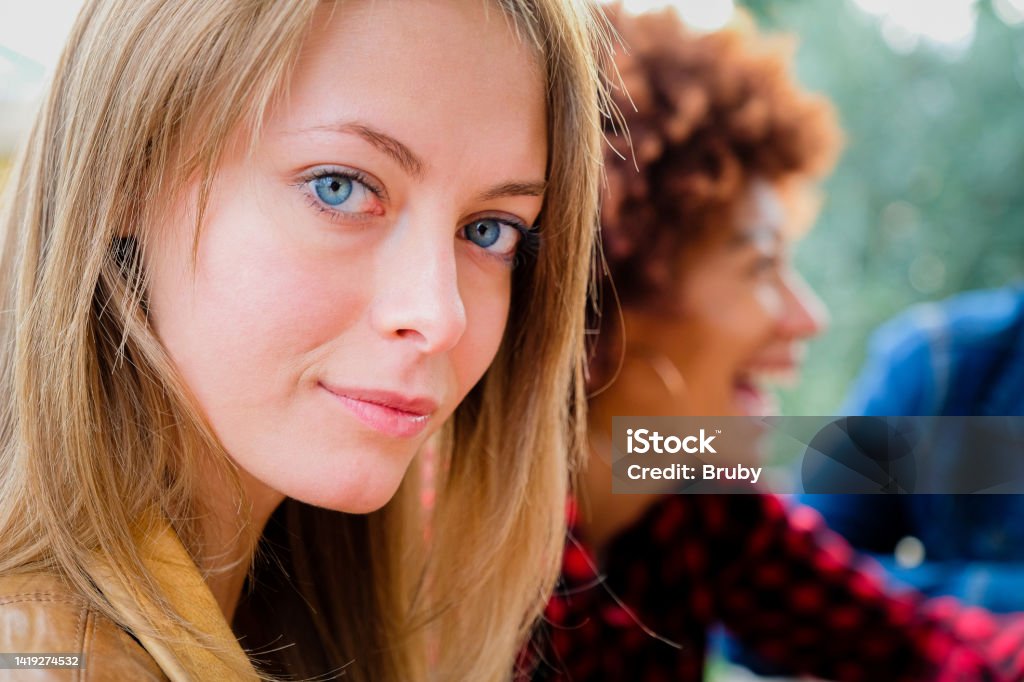 Portrait of beautiful blonde young woman looking at camera with blue eyes. Close up face of girl with friends outdoor Fun Stock Photo