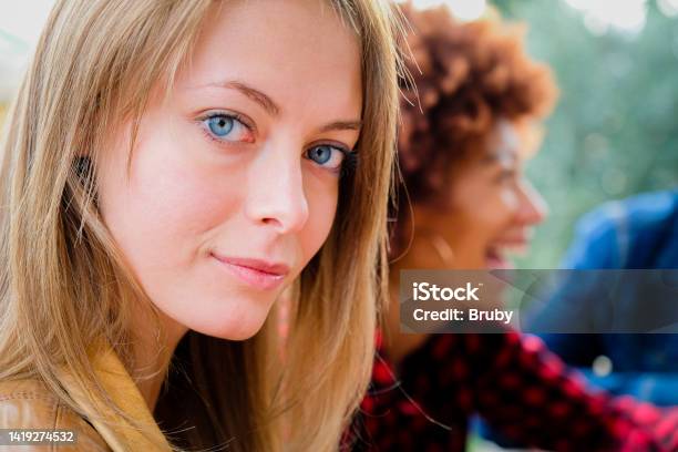 Portrait Of Beautiful Blonde Young Woman Looking At Camera With Blue Eyes Close Up Face Of Girl With Friends Outdoor Stock Photo - Download Image Now