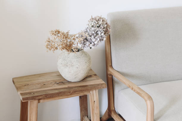 Fall still life photo. Rustic textured vase with dry hydrangea flowers on old wooden bench. Blurred linen mid century sofa background. White wall. Scandinavian interior. Boho elegant home decor. stock photo