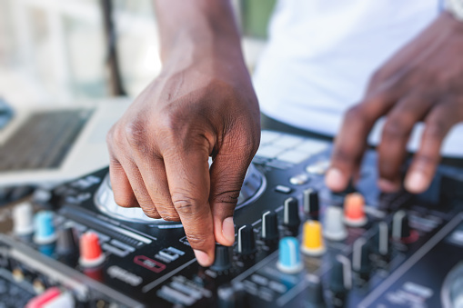 View of Dj mixer and vinyl plate with headphones on a table with african american DJ playing on stage and mixes the track in the background, during summer open air event techno party, hand close-up