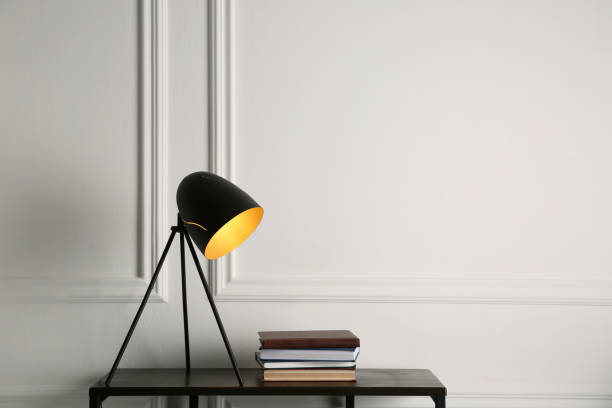 istock Wooden table with books and modern lamp near white wall, space for text. Interior element 1419277064