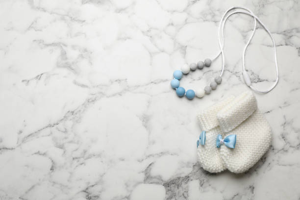 Cute baby booties and toy on white marble background, flat lay. Space for text