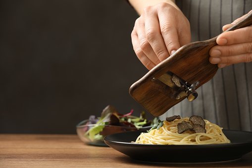 Woman slicing truffle onto spaghetti at wooden table, closeup