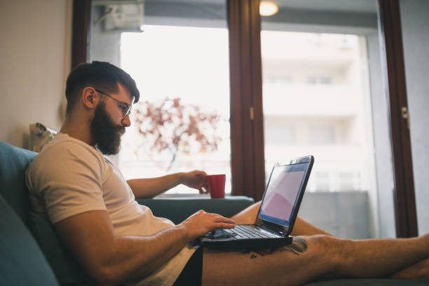 istock Handsome, hipster man sitting on the livingroom sofa, using laptop 1419281830