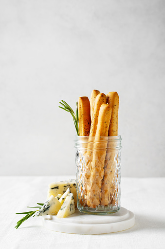 Grissini staing in glass with blue cheese, bread stick, italian traditional cuisine close up on white background, top view, vertical