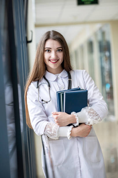 istock happy young nurse in uniform with stethoscope smiling in corridor. 1419283132