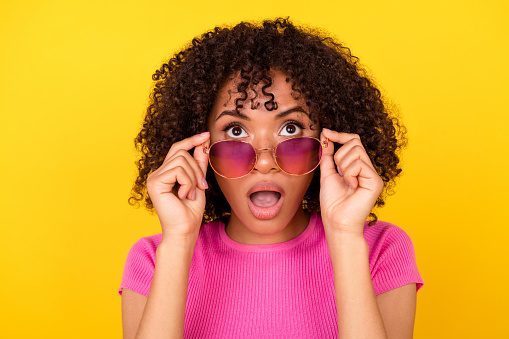 Photo of excited pretty lady wear pink top arms dark eyewear looking empty space isolated yellow color background.