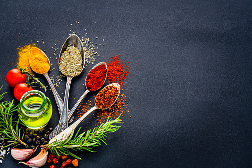 Culinary background: overhead view of herbs and Indian spices arranged at the left of black background leaving useful copy space for text and/or logo at the left. High resolution 42Mp studio digital capture taken with Sony A7rII and Sony FE 90mm f2.8 macro G OSS lens