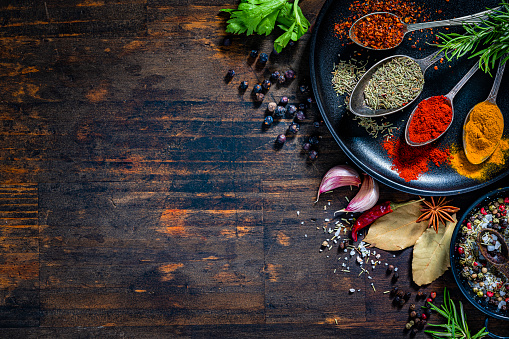 Culinary background: overhead view of herbs and spices arranged at the right of a rustic wooden table background leaving useful copy space for text and/or logo at the left. High resolution 42Mp studio digital capture taken with Sony A7rII and Sony FE 90mm f2.8 macro G OSS lens