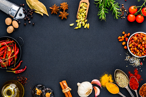 Variety of herbs and spices on slate background. Many are held on metal and wooden spoons. There is also a chilli pepper.