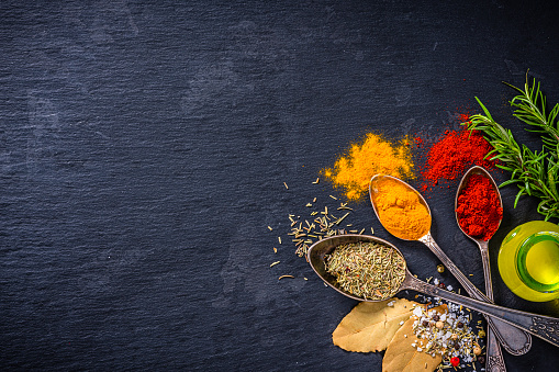Culinary background: overhead view of herbs and Indian spices arranged at the botton right of black background leaving useful copy space for text and/or logo at the left. High resolution 42Mp studio digital capture taken with Sony A7rII and Sony FE 90mm f2.8 macro G OSS lens