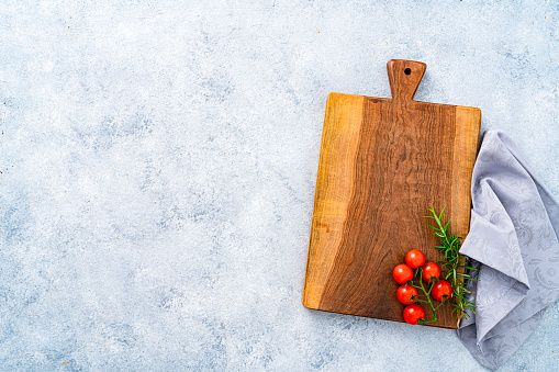 Culinary background: overhead view of a wooden cutting board with a gray fabric napkin, cherry tomatoes and rosemary. The composition is at the right of an horizontal abstract gray background leaving useful copy space for text and/or logo at the left. High resolution 42Mp studio digital capture taken with SONY A7rII and Zeiss Batis 40mm F2.0 CF lens