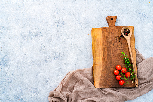 Culinary background: overhead view of a wooden cutting board with a brown textile tablecloth, cherry tomatoes, peppercorns and rosemary. The composition is at the right of an horizontal abstract gray background leaving useful copy space for text and/or logo at the left. High resolution 42Mp studio digital capture taken with SONY A7rII and Zeiss Batis 40mm F2.0 CF lens