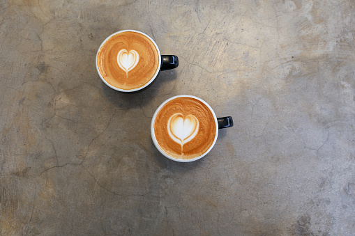 Two hot cups of cappucino on concrete background. Heart shape art latte symbol of love. Valentine's day concept