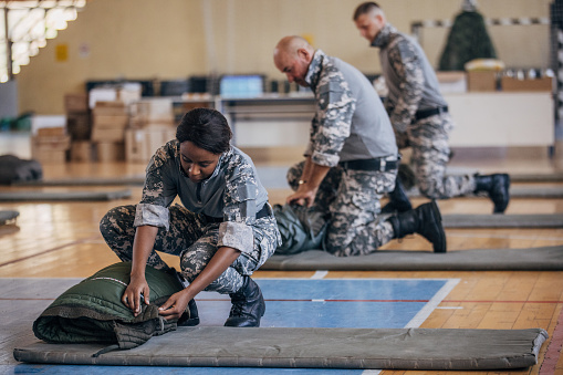 Soldiers on humanitarian aid preparing sleeping bags for civilians in school gymnasium, after natural disaster happened in city.