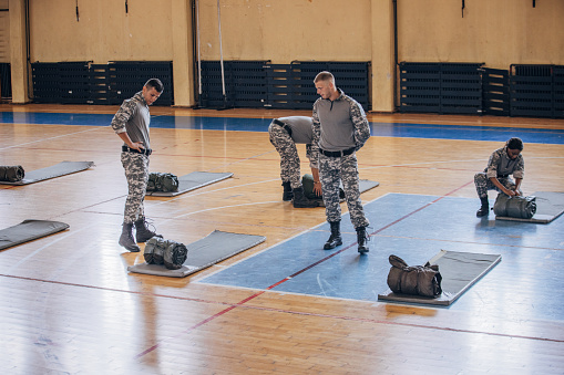 Soldiers on humanitarian aid preparing sleeping bags for civilians in school gymnasium, after natural disaster happened in city.