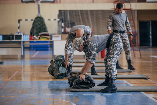Soldiers on humanitarian aid preparing sleeping bags for civilians in school gymnasium, after natural disaster happened in city.