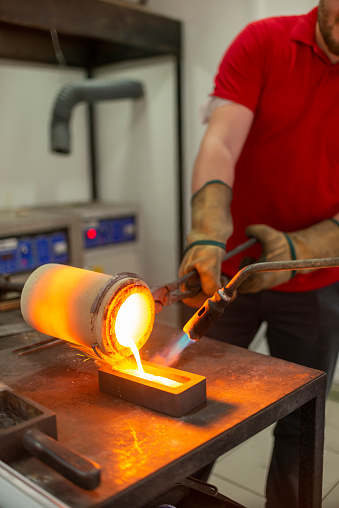 Smelted gold being poured by an experienced gold refiner from the crucible into a mold.