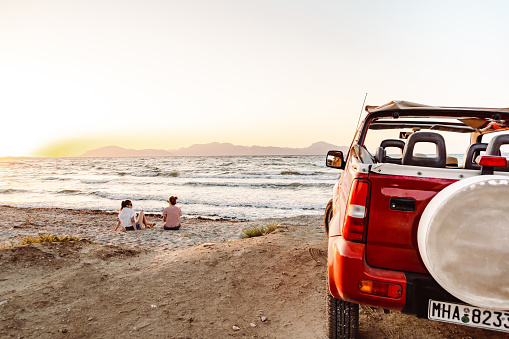 Two happy young women enjoying a summer’s road trip. They are looking at the view and enjoy while sitting on the beach