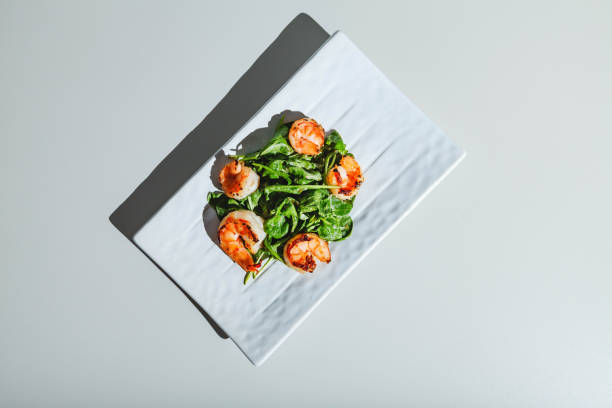 Salad with shrimps and arugula on white dish on white background. Hard light, deep shadow