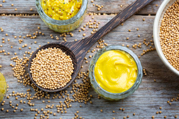 different types of mustard and mustard seeds on a rustic wooden board - mosterdplant stockfoto's en -beelden