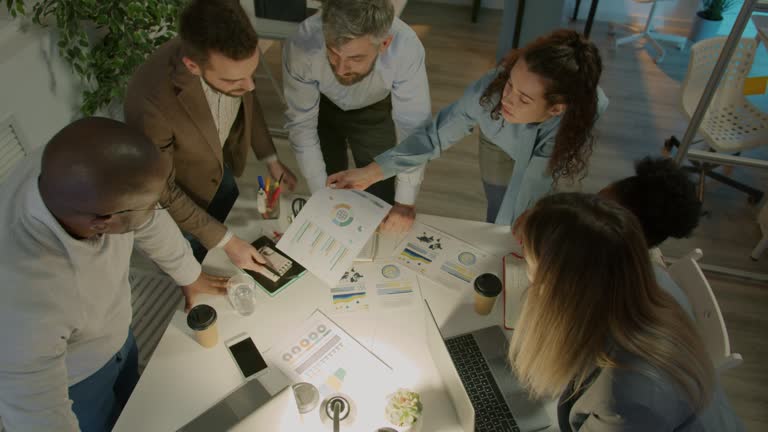 High angle view of business team studying charts and discussing project in office in the evening