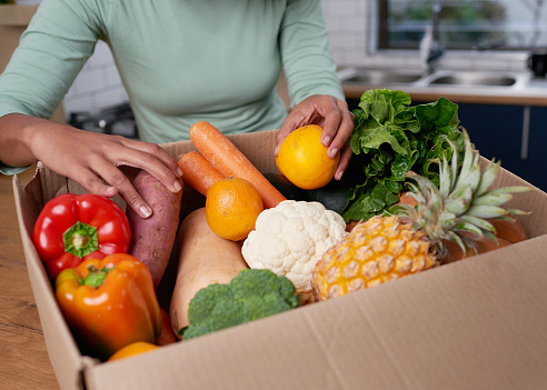 An anonymous young woman checks her fruit and veg delivery box. High quality photo