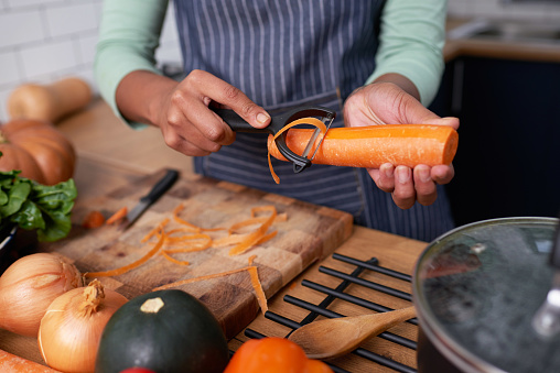 Close up of young woman's hands peeling carrots for vegan soup or stew. High quality photo