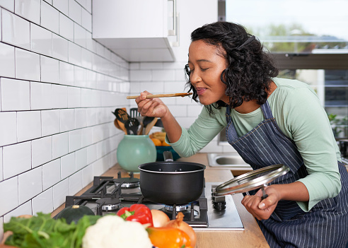 A young multi-racial woman smells and tastes her cooking on the stove. High quality photo