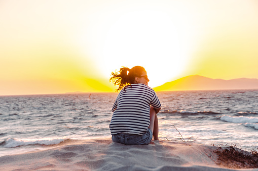 Woman in shorts and stripped shirt sitting on the beach and enjoying the sunset.