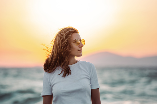 Woman in white shirt standing by the sea with a wind in her hair