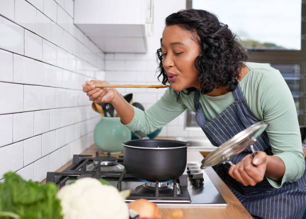 A young multi-racial woman smells and tastes her cooking on the stove stock photo
