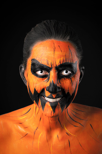 A portrait of a woman smiling in creepy Halloween jack o' lantern face paint.