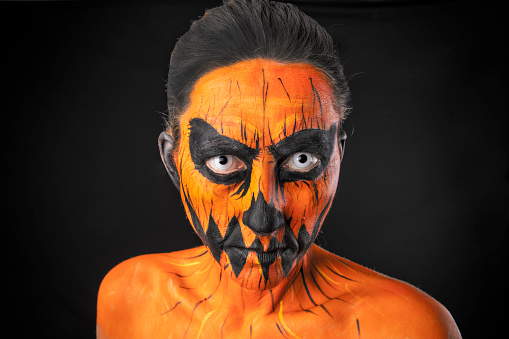 A woman painted as a creepy jack o' lantern.