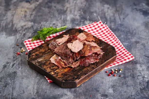 Pieces of baked meat on cutting board on gray background.