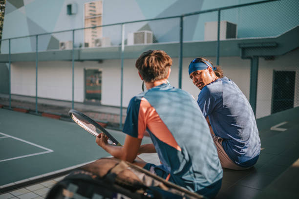 2 azjatyckich zawodowych tenisistów lubi rozmawiać siedząc na bleachers na korcie tenisowym, robiąc sobie przerwę po treningu rano - tennis men vitality joy zdjęcia i obrazy z banku zdjęć