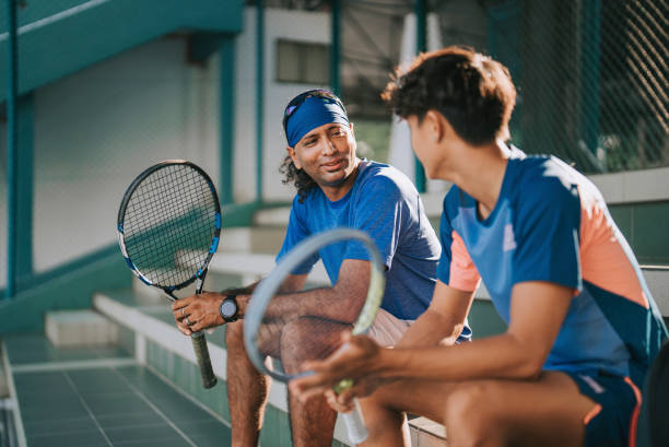 2 azjatyckich zawodowych tenisistów lubi rozmawiać siedząc na bleachers na korcie tenisowym, robiąc sobie przerwę po treningu rano - tennis men vitality joy zdjęcia i obrazy z banku zdjęć