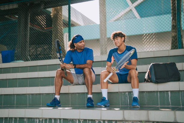 2 azjatyckich zawodowych tenisistów lubi rozmawiać siedząc na bleachers na korcie tenisowym, robiąc sobie przerwę po treningu rano - tennis men vitality joy zdjęcia i obrazy z banku zdjęć