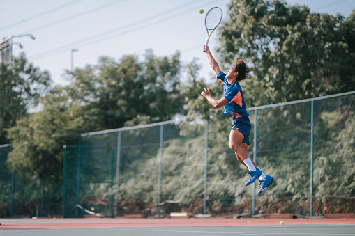 Asian Chinese male professional tennis player jumping mid air serving in hardcourt