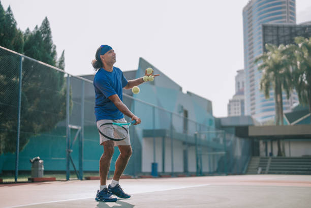 아시아 남자 테니스 코치가 주말 아침에 하드 코트에서 학생 훈련 수업에 테니스 공을 전달합니다. - tennis asian ethnicity male forehand 뉴스 사진 이미지