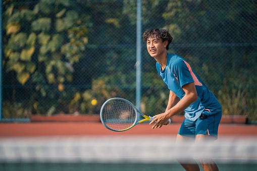 Cheerful Chinese young male tennis player smiling at hardcourt practicing