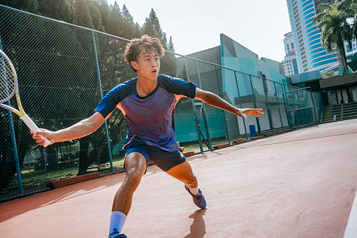 aggressive asian Chinese male tennis player aiming to hit tennis ball in hardcourt tennis competition