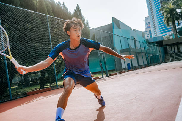 aggressive asian Chinese male tennis player aiming to hit tennis ball in hardcourt tennis competition stock photo