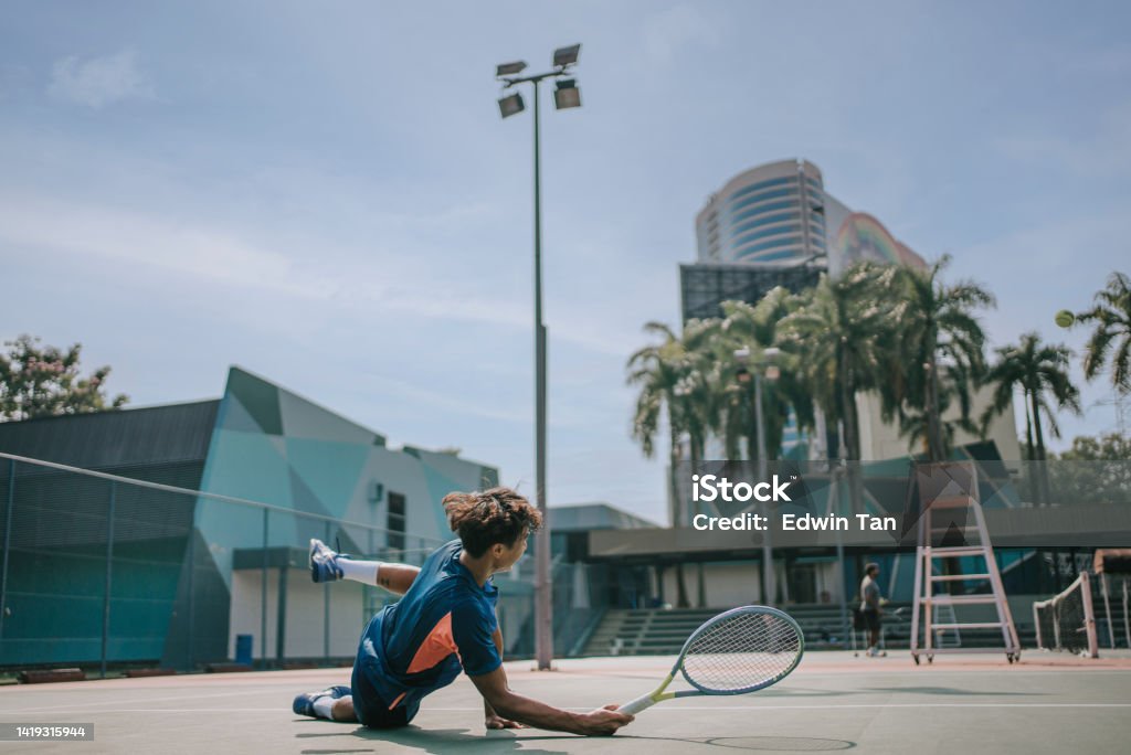 Asian Chinese male tennis player fell on floor try making a save in hardcourt Falling Stock Photo