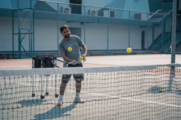 인도 남자 테니스 코치는 하드 코트 일상적인 주말 아침 수업에서 학생에게 테니스 공을 던지는 서비스를 제공합니다. - tennis asian ethnicity male forehand 뉴스 사진 이미지