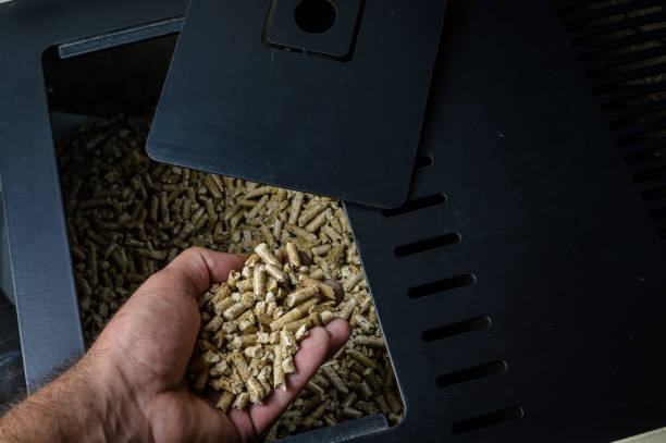 hand holding wood pellets going into the stove compartment, alternative heating energy solution hand holding wood pellets going into the stove compartment, alternative heating energy solution wood burning stove stock pictures, royalty-free photos & images
