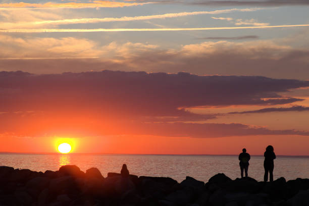 istock Silhouettes of unrecognizable people on breakwater rocks viewing dramatic Cape Cod sunset 1419325023