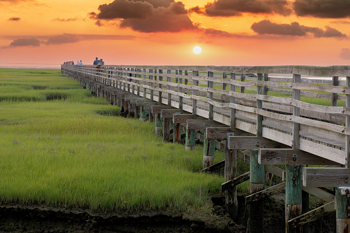 Scenic view of colorful Cape Cod sunset over long raised wooden boardwalk spanning saltwater marsh at Grays Beach, Yarmouth Port, Massachusetts.